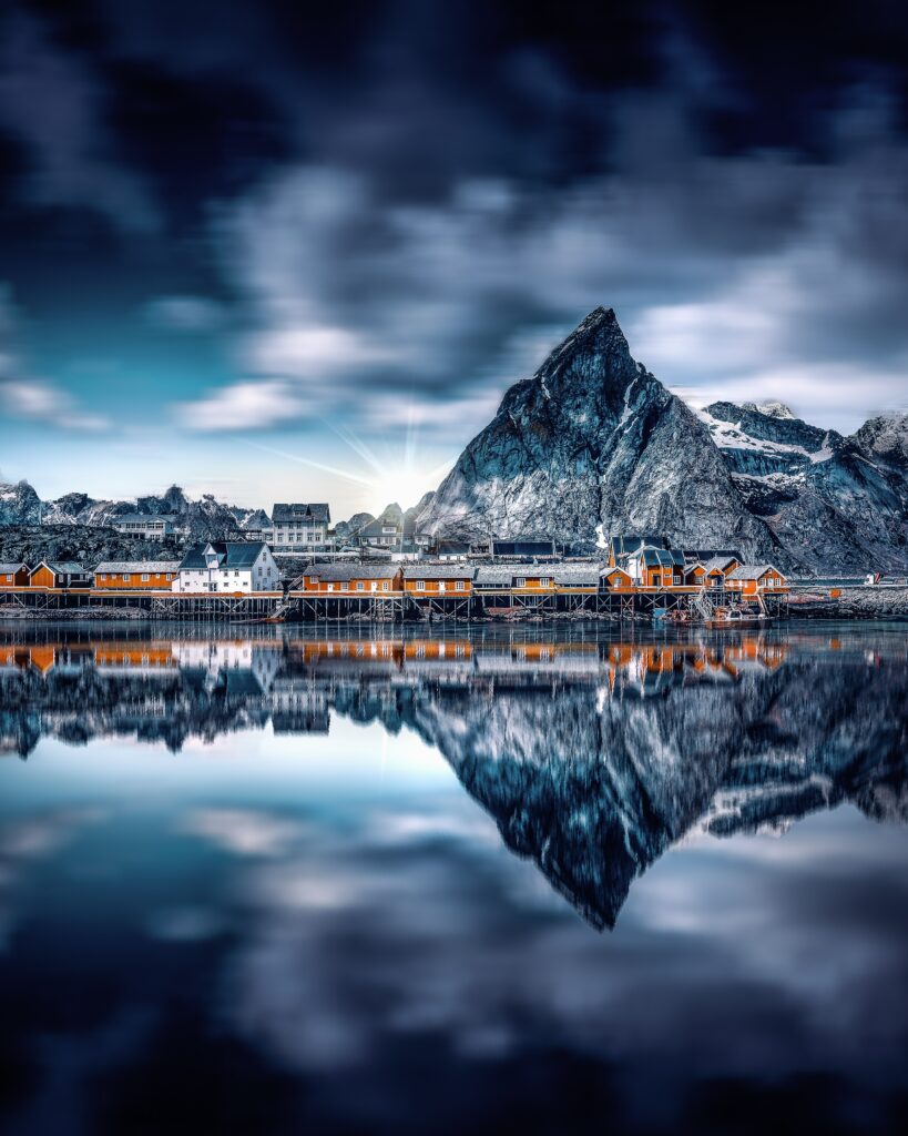 Serene lakeside village beneath towering mountain peaks reflected in still blue water wallpaper