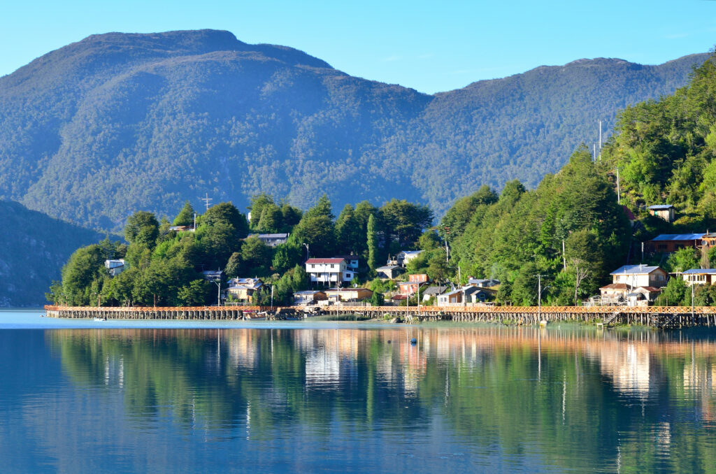 Tranquil lakeside village with colorful buildings reflected in calm blue lake and mountains Wallpaper