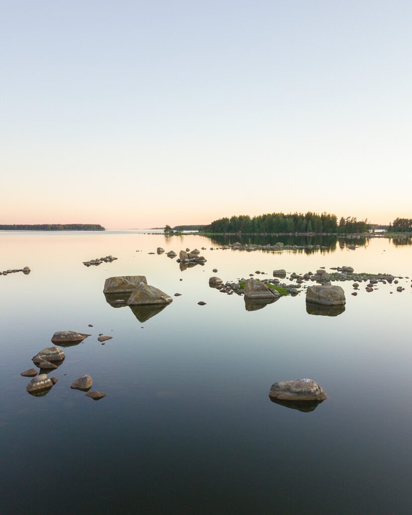 Serene lakeside wallpaper with smooth stones calm water pastel sky lush green trees horizon