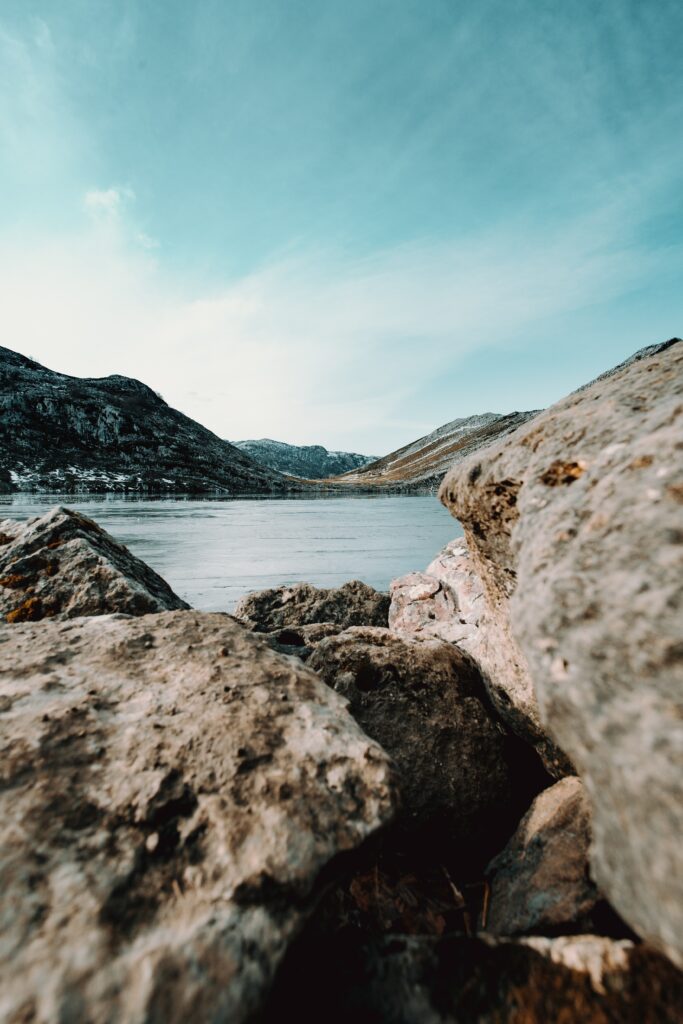 Serene lakeside with rugged rocks calm still water pale blue sky natural earthy tones wallpaper