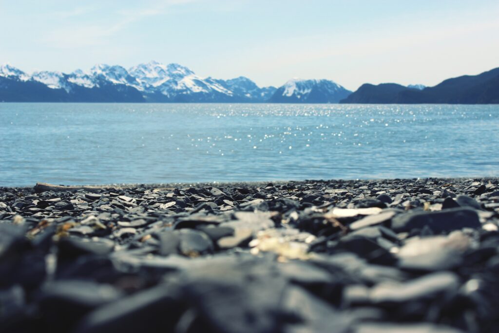 Serene lakeside with smooth grey rocks clear water and snow-capped mountains under blue sky wallpaper