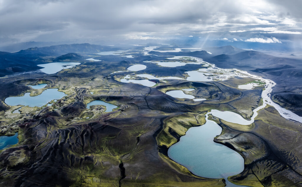 Expansive plain with lakes rivers and rugged mountains under dramatic cloudy sky nature wallpaper
