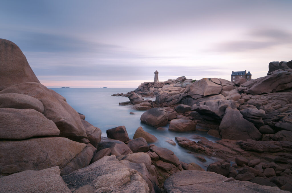 Lone lighthouse on rocky cliffs with calm sea and pastel sky peaceful coastal wallpaper background