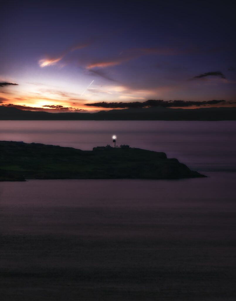 Lone lighthouse on rugged cliff at sunset with calm sea and vibrant orange purple sky wallpaper background