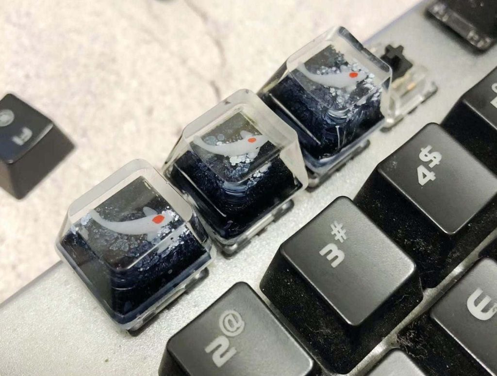 Macro shot of custom resin keycaps with white koi fish in glittery blue water for gaming setup Wallpaper