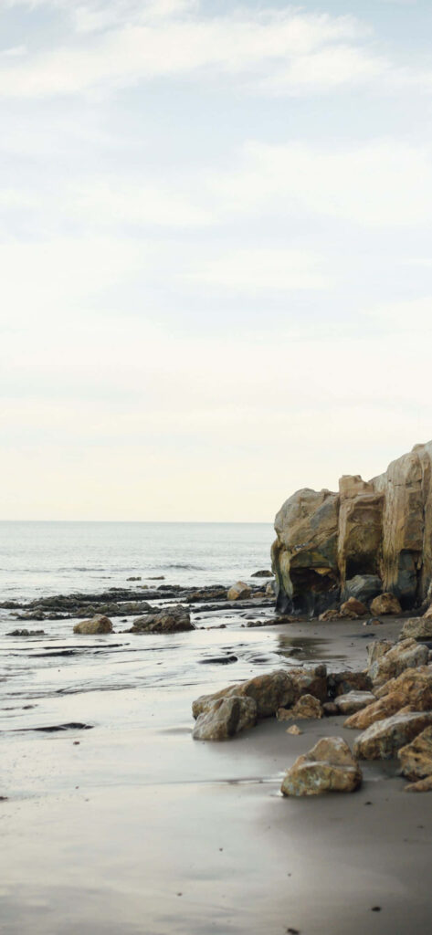 Serene Malibu Beach: Rugged Rocks & Gentle Waves Under Pastel Sky Wallpaper
