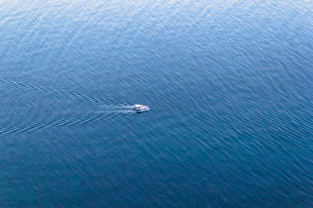 Small boat sails on calm blue sea leaving gentle trail serene minimalist nature wallpaper background