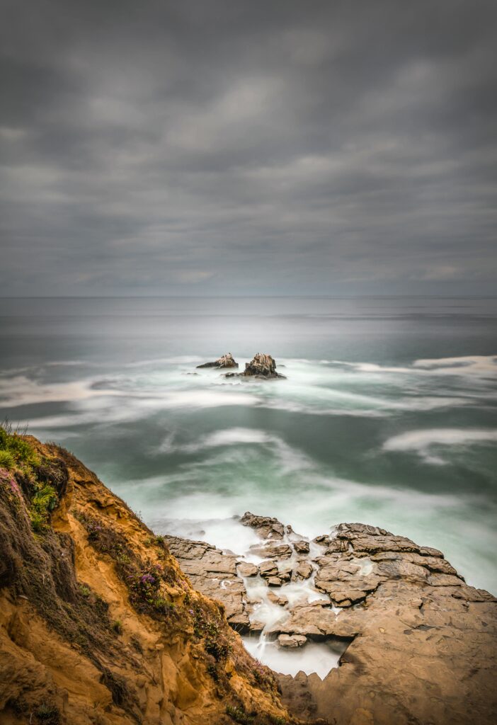 Tranquil seascape with rugged rocks misty waves foggy sky earthy tones serene nature wallpaper