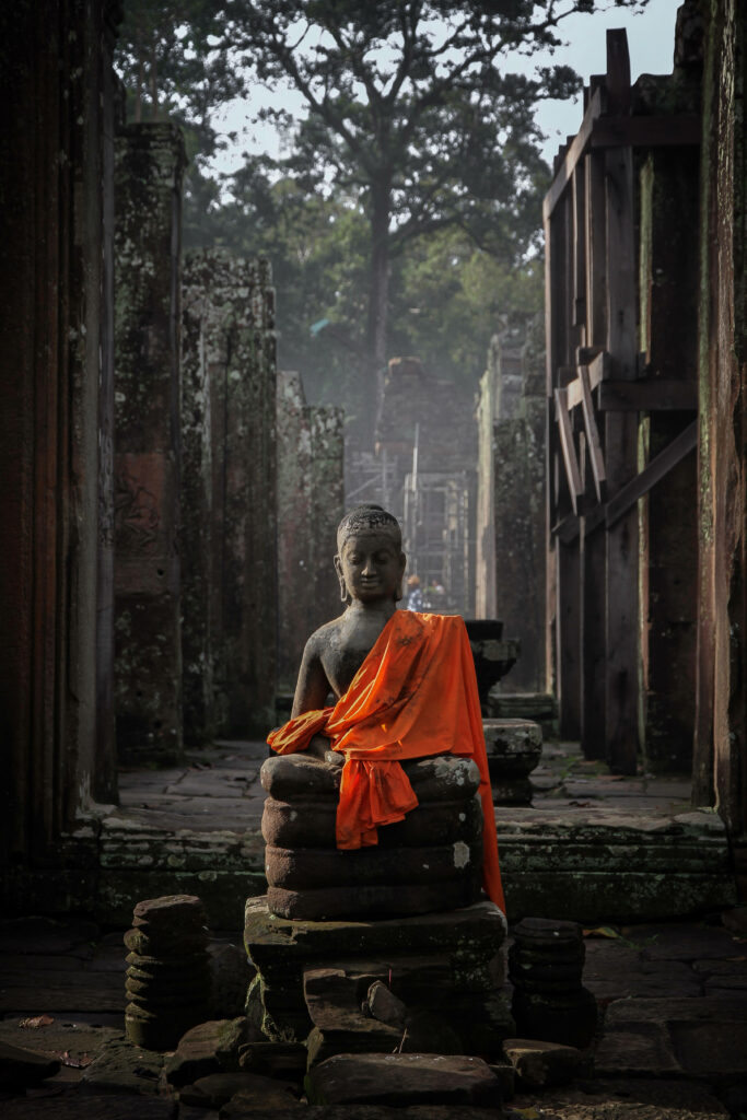 Serene monk statue in orange robe sitting peacefully among ancient stone ruins of Angkor Wat Wallpaper