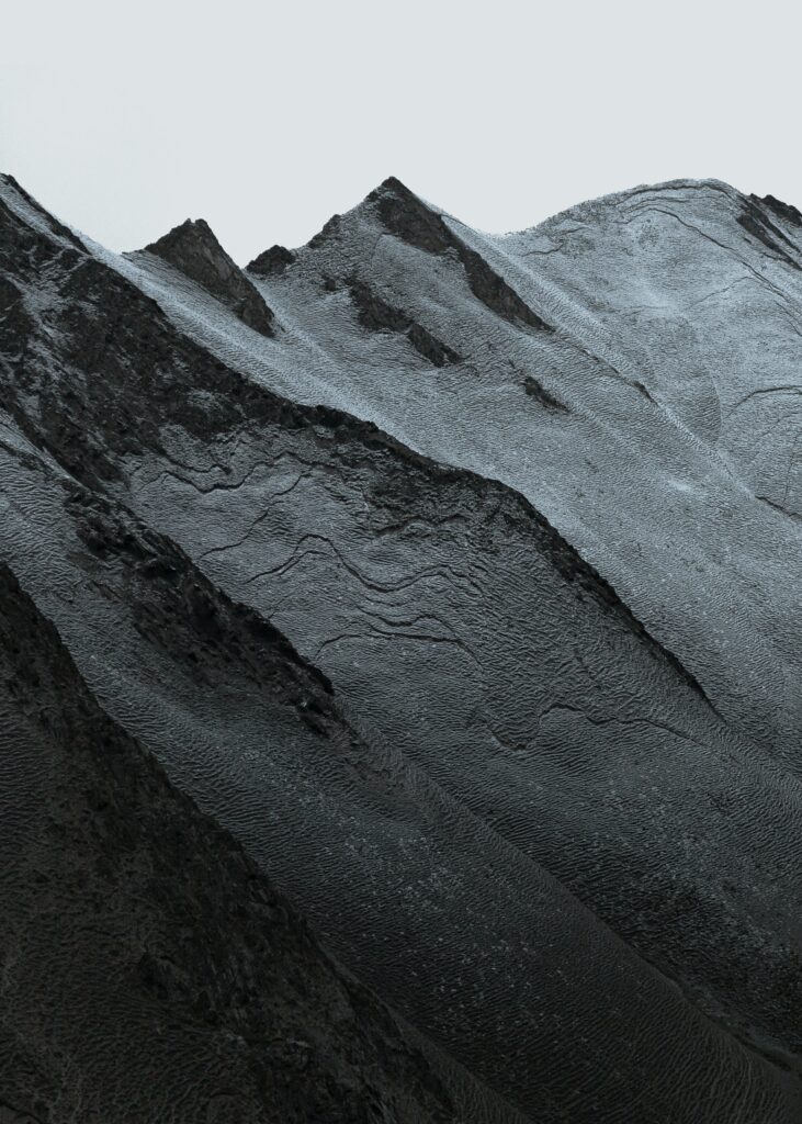 Rugged mountain slopes and sharp peaks under pale sky in a serene monochrome landscape wallpaper