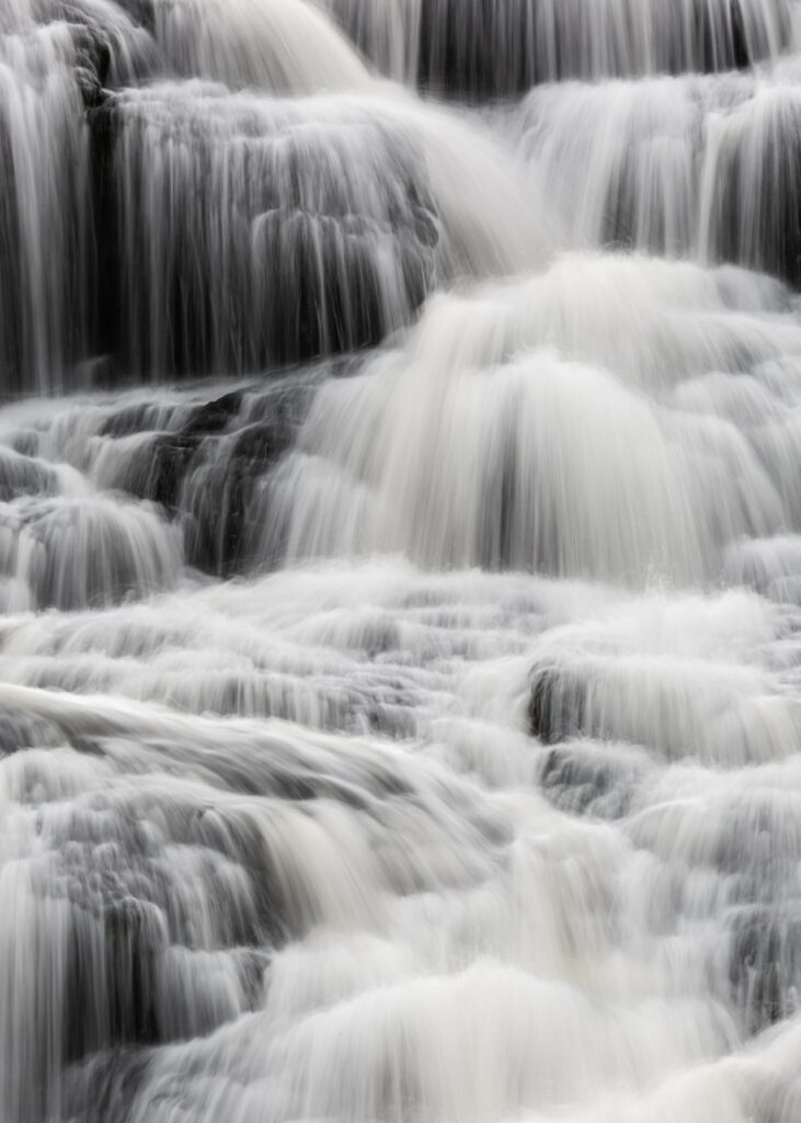 Monochrome waterfall flowing over textured dark rocks creating serene nature wallpaper background