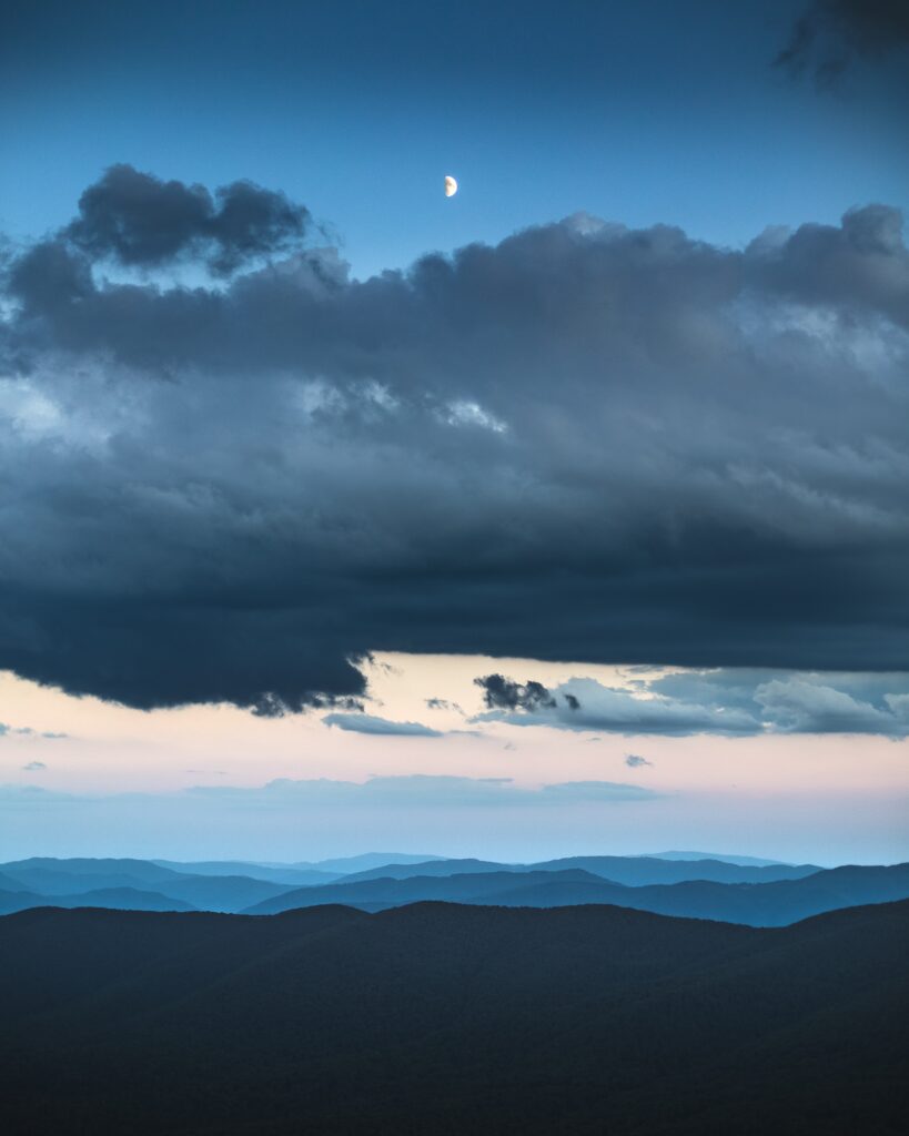 Serene moon over misty blue hills with layered clouds creating a tranquil evening landscape Wallpaper