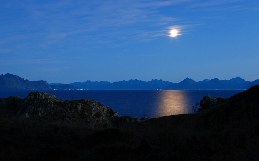 Glowing moon reflecting on calm water with rugged mountains under tranquil night sky wallpaper