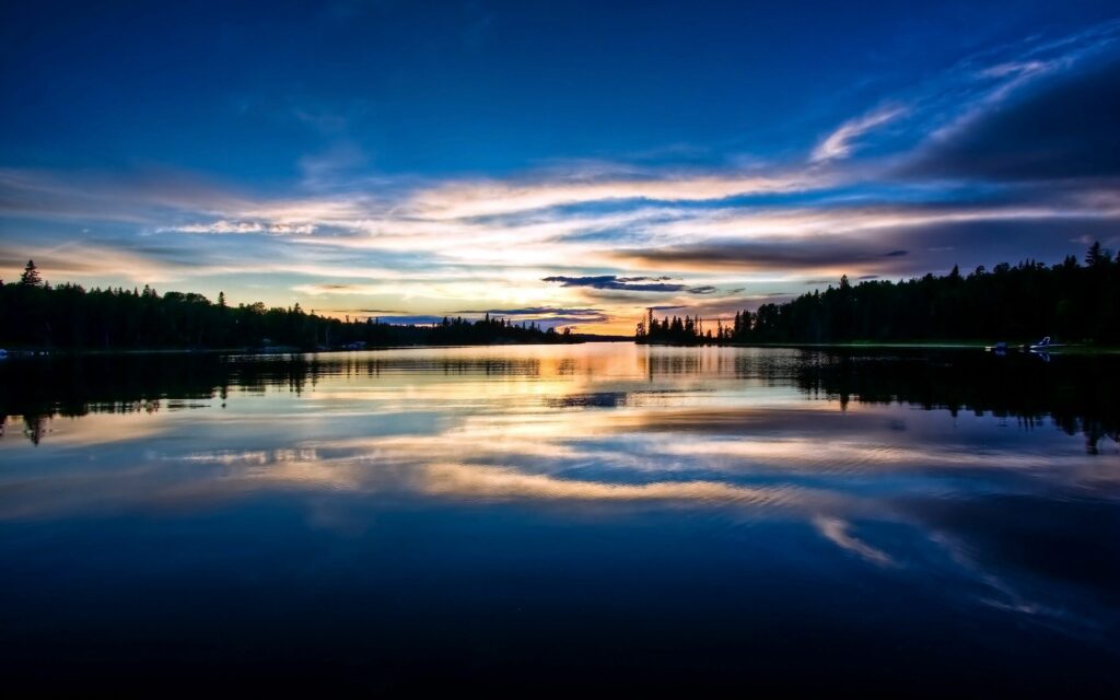Serene morning lake with clear water reflecting vibrant sky and soft clouds peaceful wallpaper