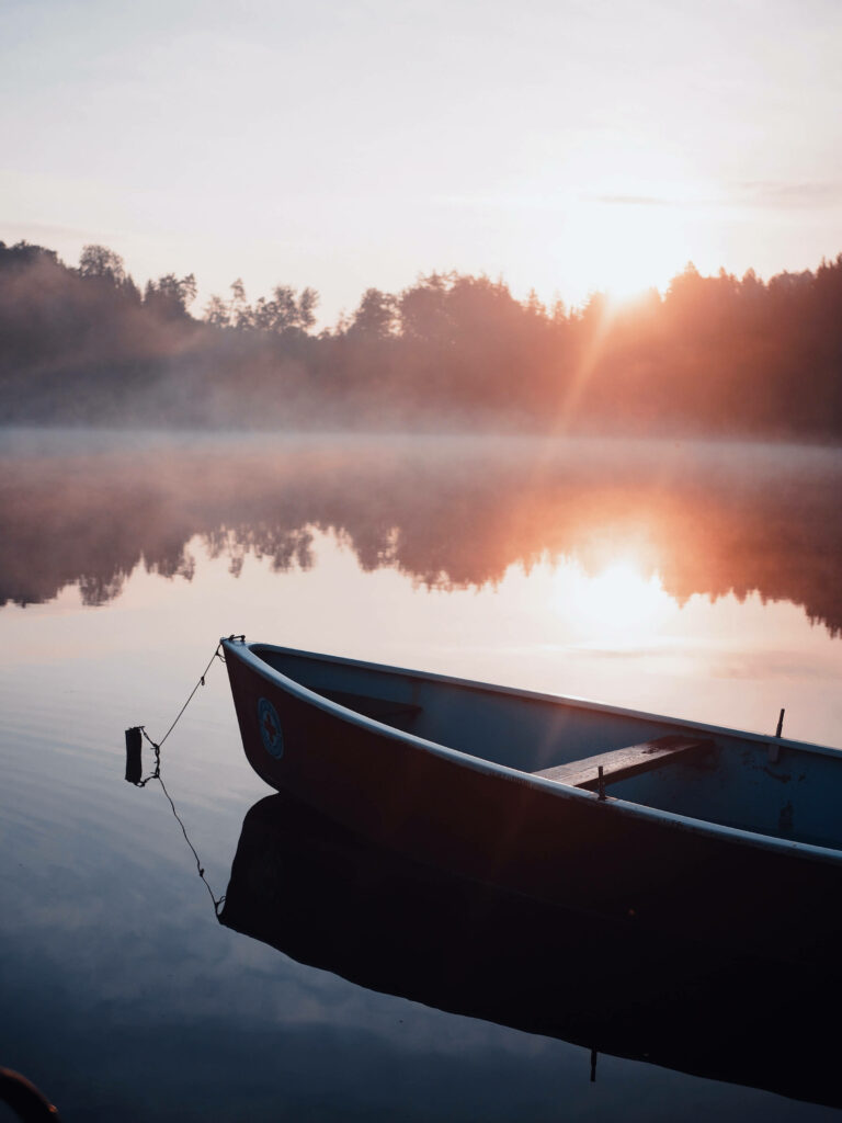 Peaceful boat on calm lake with morning sunlight reflecting on still water serene wallpaper background