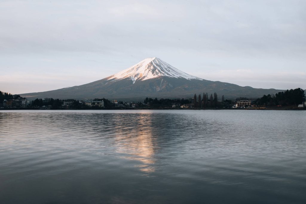 Snow-capped Mount Fuji reflected in calm lake under soft light serene Japan wallpaper background