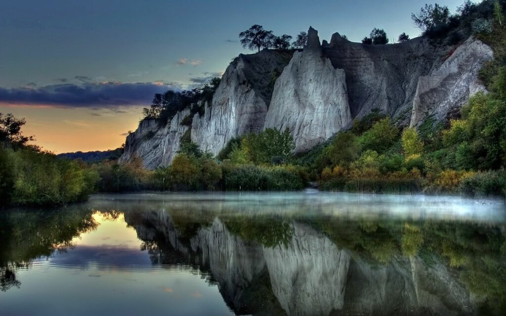 Tranquil mountain cliffs reflected on smooth water with lush trees serene nature wallpaper background