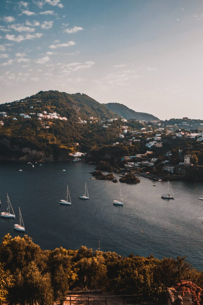 Aerial view of serene mountains with boats on lake near vibrant town and lush greenery wallpaper
