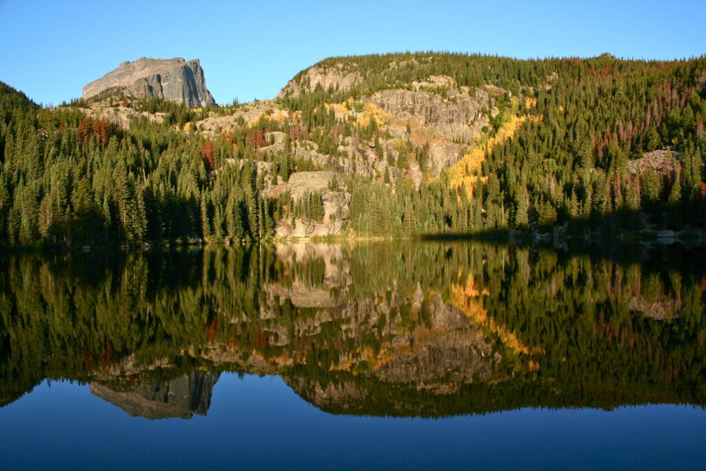Serene mountain lake reflecting green golden forest rocky cliffs and clear blue sky wallpaper