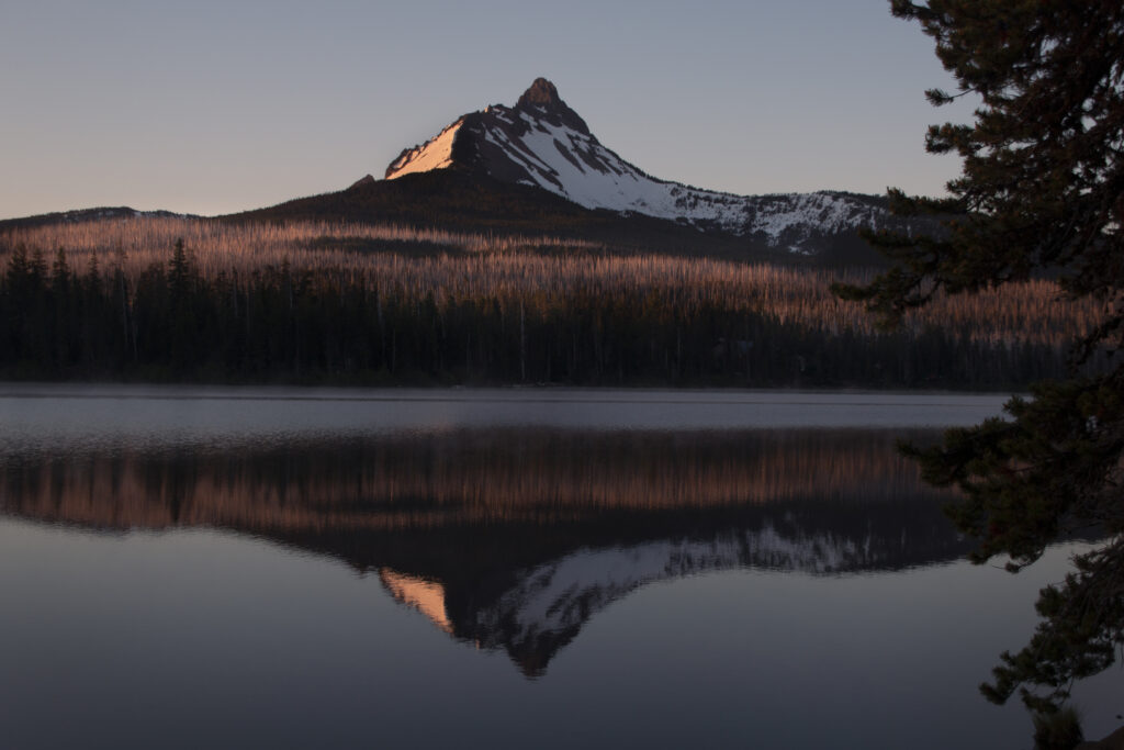 Serene mountain peak reflected in clear lake surrounded by dense forest at twilight wallpaper