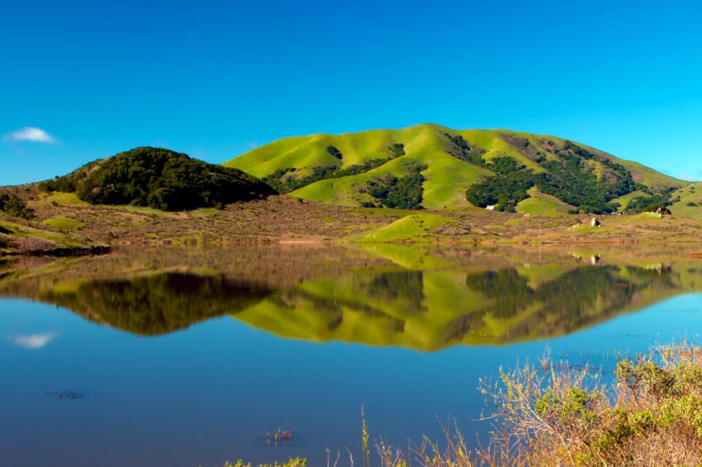 Serene lake with clear water reflecting green mountains and blue sky high resolution wallpaper