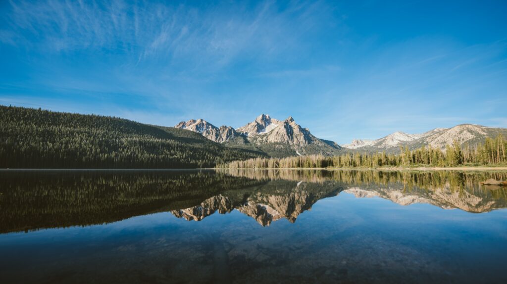 Serene lake reflecting majestic mountain range and lush green forest under clear blue sky wallpaper