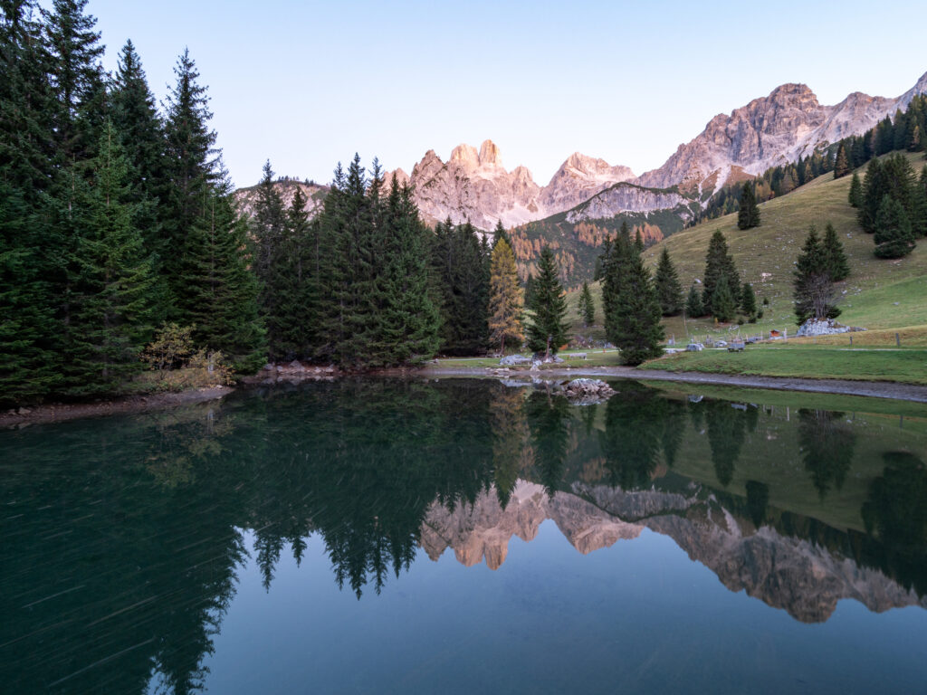 Serene mountain landscape with jagged rocks reflected in still lake surrounded by green pines Wallpaper