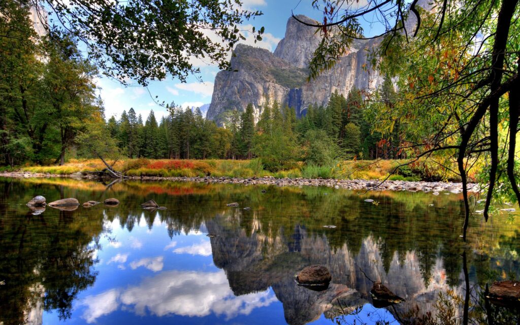 Serene lake with smooth stones lush greenery and mountain reflections on calm water wallpaper