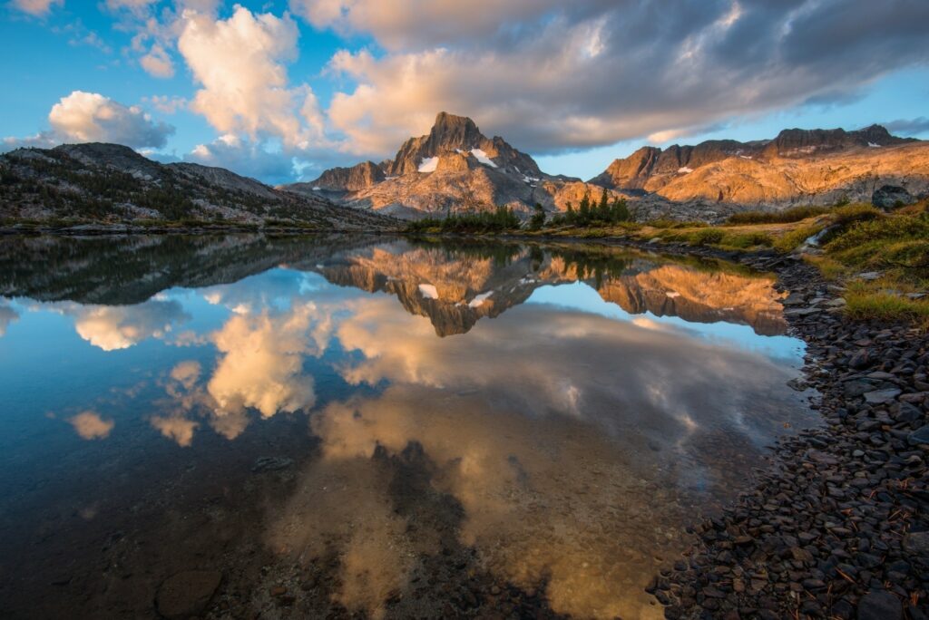 Serene mountain lake at sunrise with rugged peaks rocky shores and vivid blue sky reflection Wallpaper