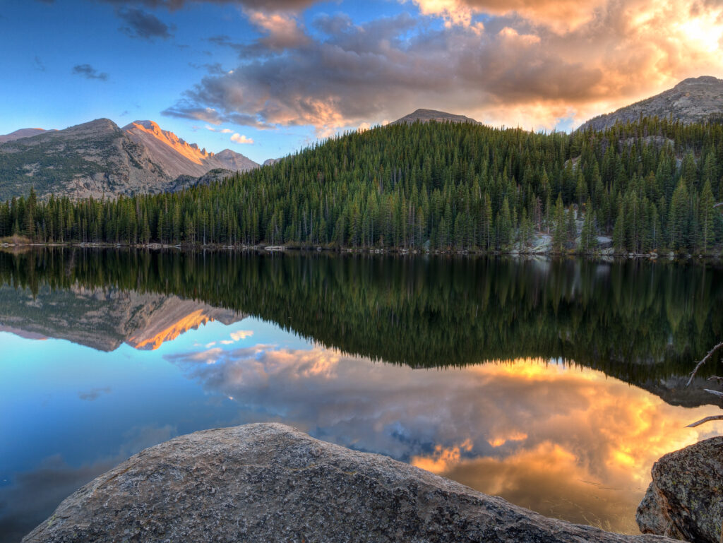Tranquil lake with evergreen forests and mountain peaks reflecting vibrant sunset sky wallpaper
