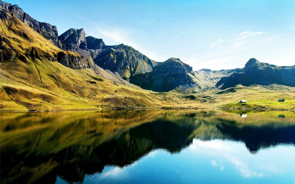 Serene mountain lake with clear water reflecting green peaks and bright blue sky wallpaper background