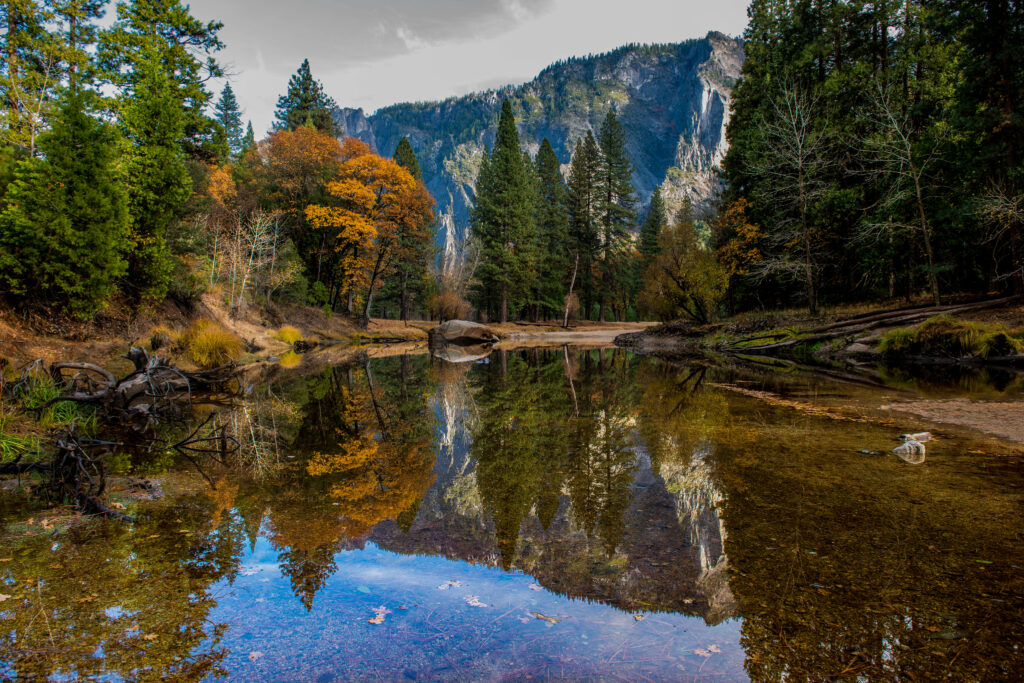 Tranquil lake with vibrant autumn trees and mountain waterfall reflecting serene nature scene Wallpaper