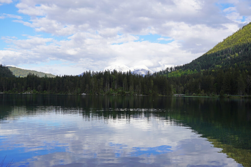 Serene lake with forest and mountains reflected on calm water under a partly cloudy sky wallpaper