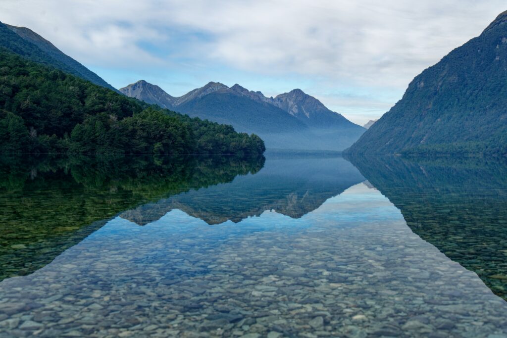Serene mountain landscape with lush trees and smooth stones reflected on clear lake water wallpaper