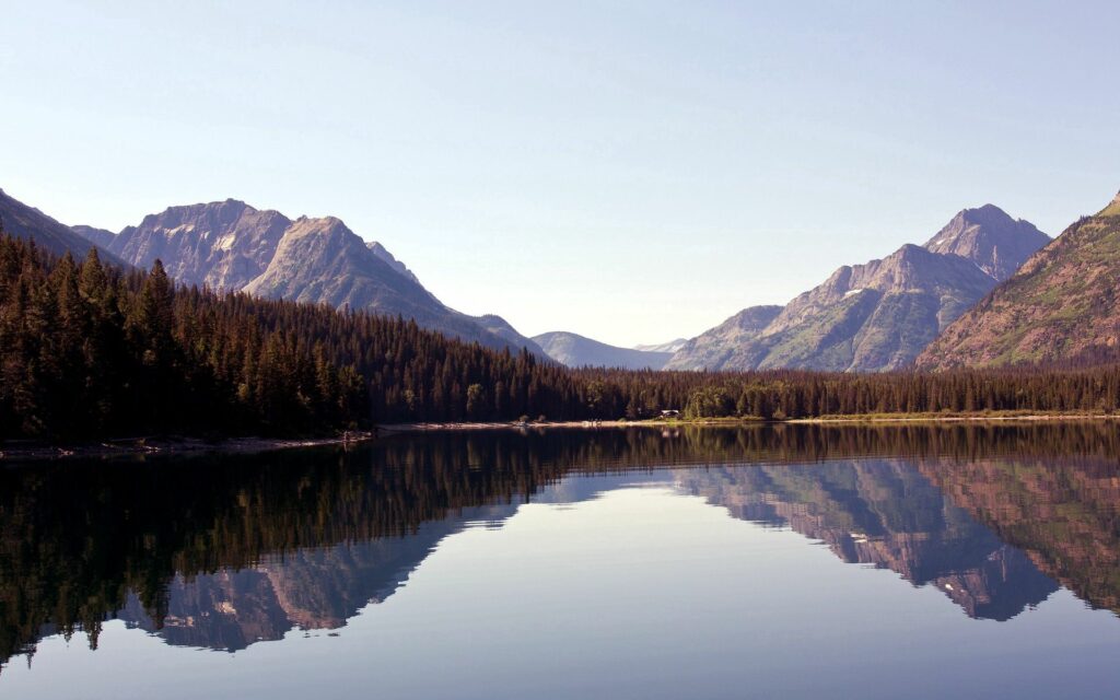 Serene lake reflecting mountains and dense trees under clear sky natural landscape wallpaper