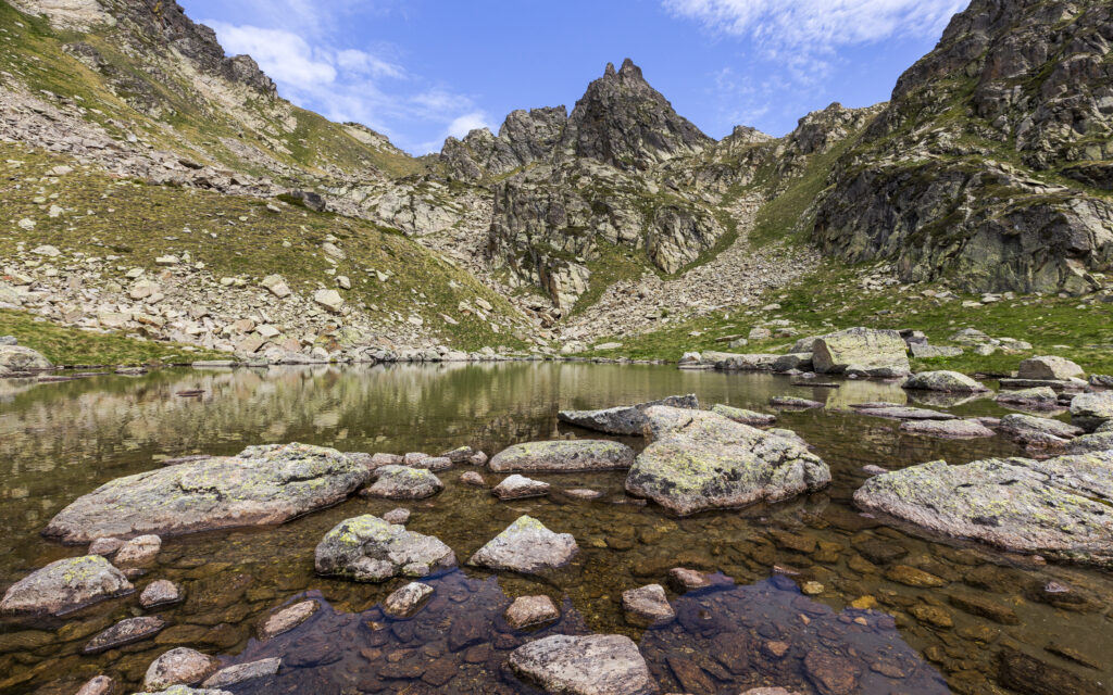 Serene mountain landscape with rocky shores and clear lake reflecting blue sky and peaks Wallpaper