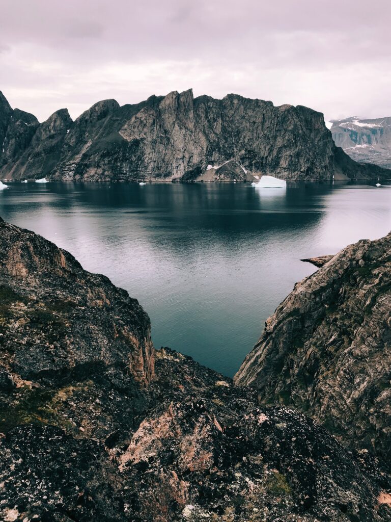 Rugged mountain landscape with rocky shore and calm lake under overcast sky wallpaper background
