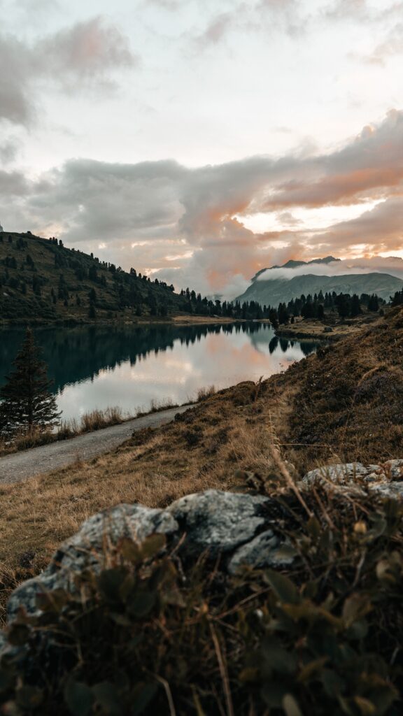 Serene mountain lake with lush trees and warm sunset clouds in soft earthy colors wallpaper
