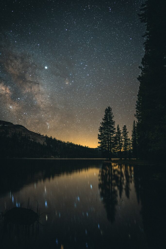 Serene lake reflecting pine trees and mountains under a starry night sky tranquil landscape Wallpaper
