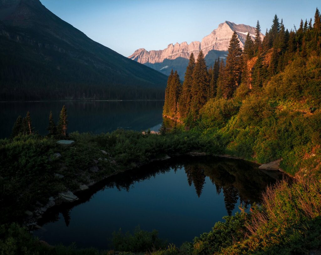 Serene mountain lake reflecting spruce trees and sunset-lit peaks in high-resolution nature scene Wallpaper