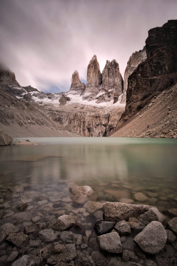 Serene mountain lake in rugged valley with cliffs smooth stones and overcast sky background Wallpaper
