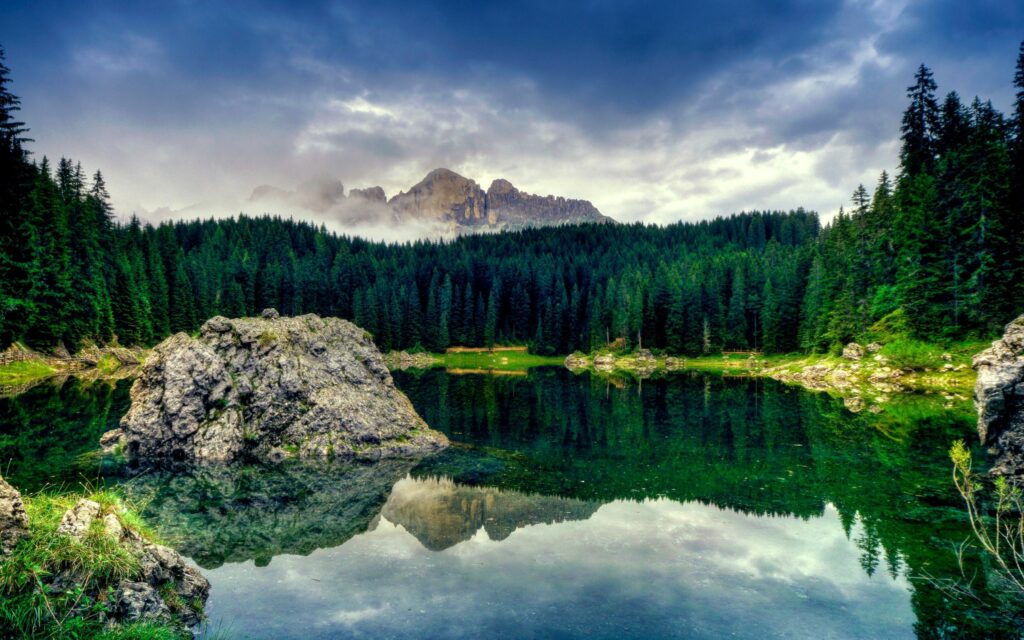 Serene mountain lake with large stone block lush conifer woods majestic mountains reflections Wallpaper
