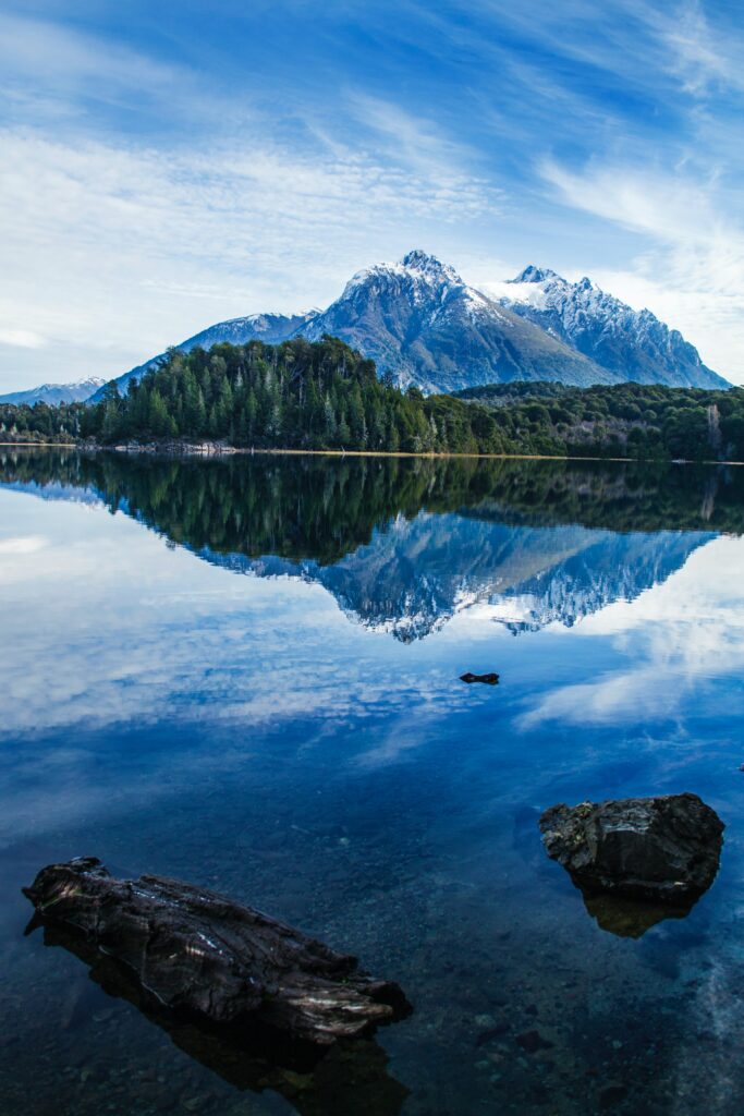 Serene mountain landscape with snow-capped peaks reflected in lake surrounded by green forest Wallpaper