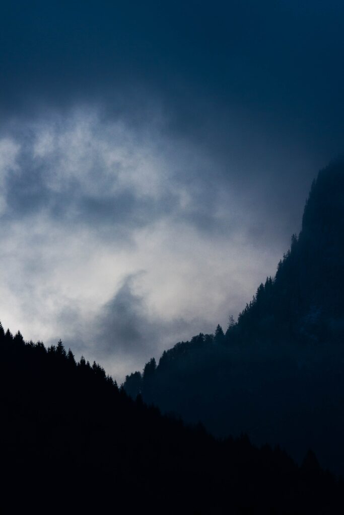 Serene mountain landscape with dark forest silhouettes and swirling dusk clouds wallpaper background