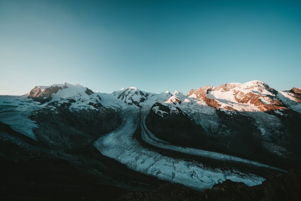 Serene mountain landscape with snowy peaks rugged rocks clear blue sky and sunlight illumination Wallpaper