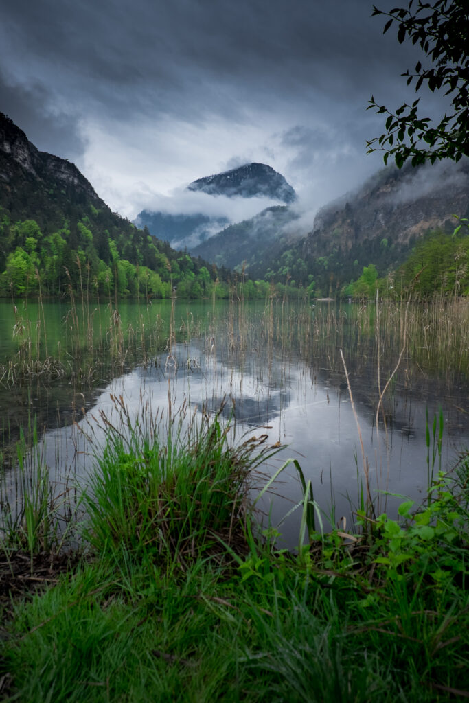 Serene mountain lake with misty peaks lush green forests and dramatic cloudy sky wallpaper background