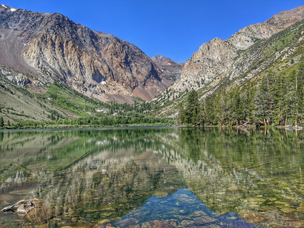 Mountain landscape with rugged slopes and dense greenery reflected on a tranquil lake Wallpaper