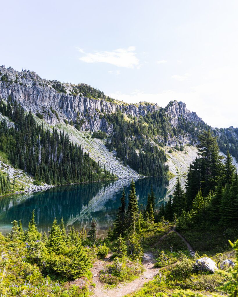 Serene mountain landscape with rocky shore dense spruce trees and clear river reflecting sky wallpaper