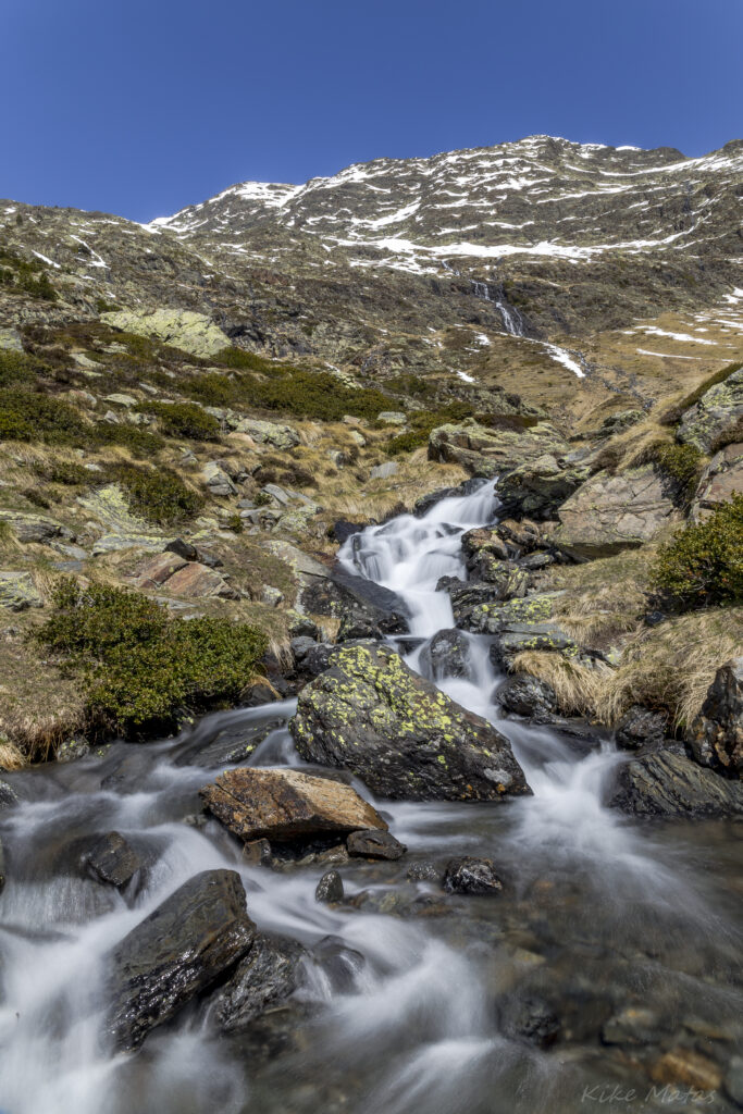 Serene mountain landscape with clear stream mossy stones snow-capped peaks blue sky wallpaper