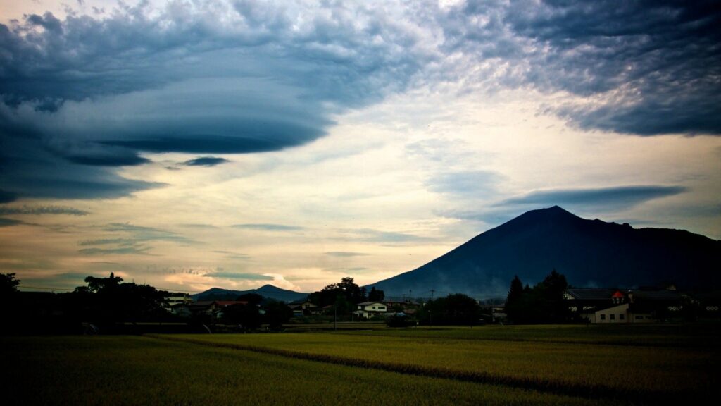 Serene mountain landscape with lush green grass and dramatic cloud-filled sky at dusk wallpaper